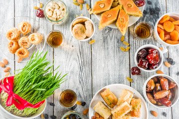 Happy Nowruz holiday background. Celebrating Nowruz sweets and treats- baklava, various dried fruits,  nuts, seeds, wooden background with green grass, copy space