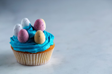 Cupcakes with blue icing with candy easter eggs on a white marble worktop