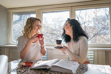 Two girls are drinking coffee and laughing in cafe