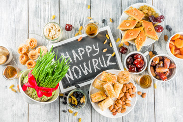Happy Nowruz holiday background. Celebrating Nowruz sweets and treats- baklava, various dried fruits,  nuts, seeds, wooden background with green grass, copy space
