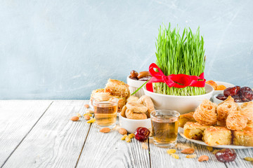 Happy Nowruz holiday background. Celebrating Nowruz sweets and treats- baklava, various dried fruits,  nuts, seeds, wooden background with green grass, copy space