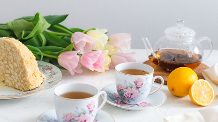 Afternoon tea with cake, lemon, teapot and tulips on the background. Tea party. Spring mood, Mother's day concept