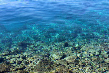 Fototapeta na wymiar Calm blue sea with clearly visible rocks on bottom going from shallow to deep end on warm sunny spring day