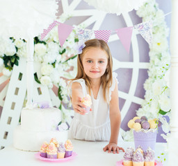Obraz na płótnie Canvas Pretty smiling little girl holding tasty cake in the beautiful decorated candy bar
