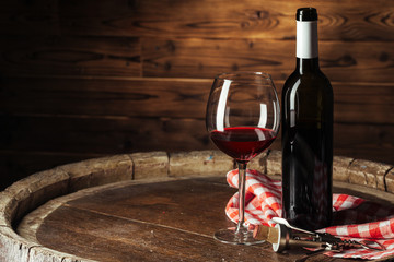 Bottle and glass of red wine on wooden barrel shot with dark wooden background