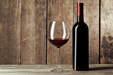 Glass and bottle with delicious red wine on table against wooden background