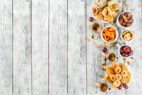 Set various Middle Eastern Arabian sweets - Turkish baklava, knafeh (kunaf), nuts, dried fruits and seeds. White wooden background, top view copy space