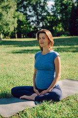 Fototapeta na wymiar Young pregnant woman practicing yoga and meditation in the park