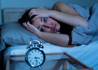 Attractive woman in bed staring at alarm clock trying to sleep feeling stressed and sleepless