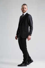 Elegant man in a three-piece suit stands in full growth on a gray background.