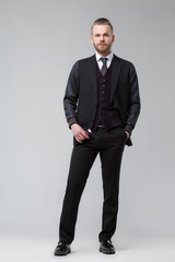 Elegant man in a three-piece suit stands in full growth on a gray background.