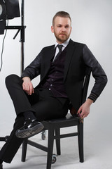 Elegant man in a three-piece suit sitting on a chair on a gray background.
