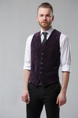 Elegant man in a vest and tie on a gray background.