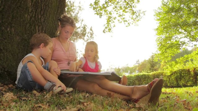 Mother and kids reading picture book in a park