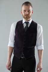 Elegant man in a vest and tie on a gray background.