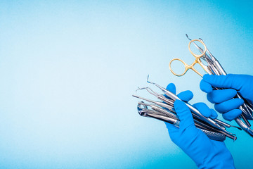 Hands in blue gloves holding surgery dental equipment on light blue background