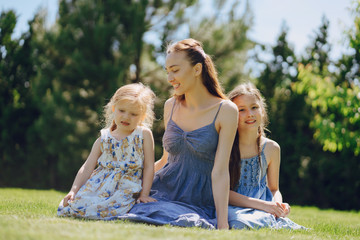 Fototapeta premium beautiful long-haired mother in a long blue dress in sunny summer forest walks with his beautiful daughters