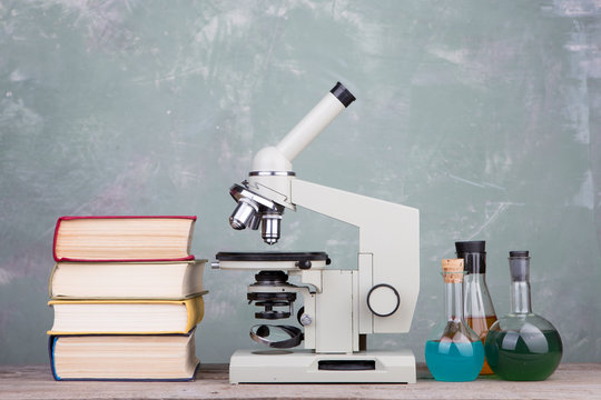 Education and science concept - books and microscope on the table on grey background