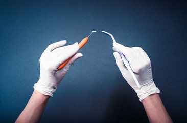 Hands in white gloves holding dental tools on dark blue background