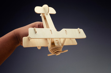 conceptual image of cropped hand holding toy wooden retro airplane on dark background