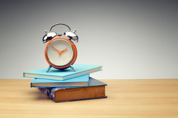 retro alarm clock on stack of book over dark background for education and time management success concept. - Powered by Adobe