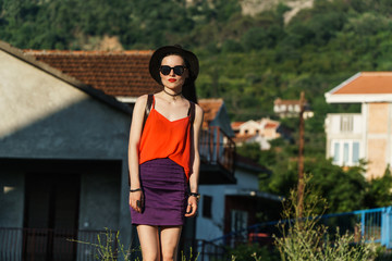 Girl in the summer in a black hat and sunglasses stands on the street