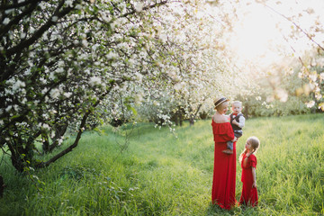 Happy stylish caucasian mother with daughter and son, walking and spending time together in blooming spring garden. Mom playing with children outdoors. Love, parenthood, childhood, happiness concept.