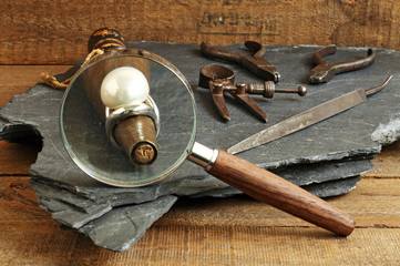 Ring, magnifying glass and jeweler tools on blackboard