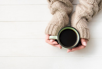 Top view of girl in sweater holding coffee mug on white table
