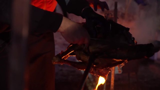 many hands cut off meat pieces from roasted pork carcass at night in slow motion