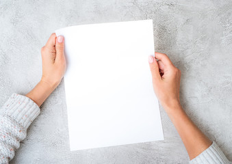 Girl's hands holding white sheet of paper vertically