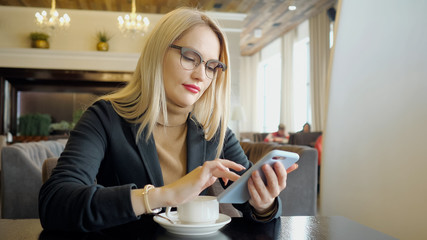 Blonde girl in suit with phone sitting at a table in a cafe, copy space. close-up