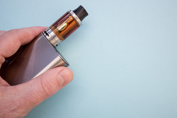 Man hand holding vape pen metal electronic cigarette with vaping blue background