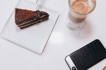 Chocolate cake with coffee latte and smartphone on white table
