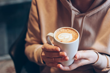 Cup of coffee cappuccino with foam heart in female hands at cafe, close up