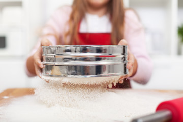 Young girl hands sifting flour with a metallic sieve - close up