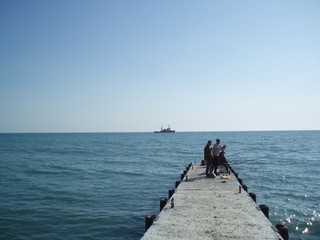 Fototapeta premium fishermen on the pier in Sochi and behind them the ship and the sea