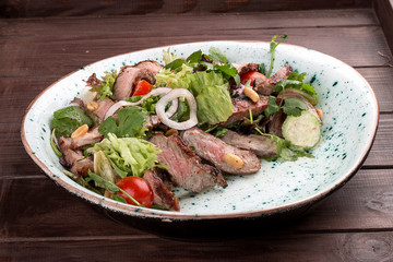 Salad with roast beef and cherry tomatoes on a wooden background