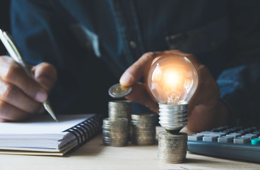 Man working with a light bulb on stack of coins for business and accounting concept.