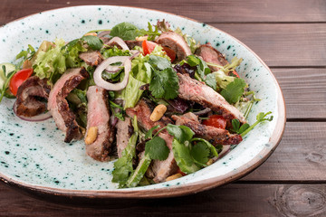 Salad with roast beef and cherry tomatoes on a wooden background