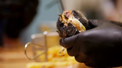 Two people in black gloves taking black burgers and eating