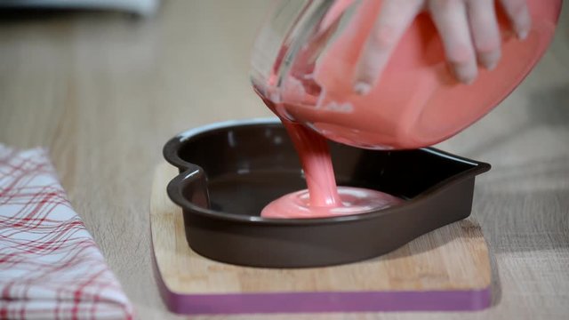 Pouring pink mousse into heart shaped molds. Confectioner making mousse cake in the kitchen.