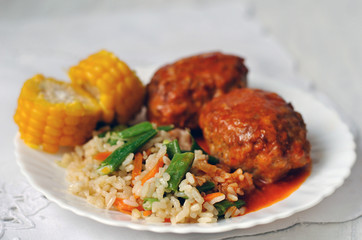 Meat cutlets with tomato sauce, rice and vegetables on a white ceramic plate. Close-up