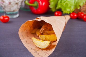 Homemade baked potato wedges with herbs with vegetables on the background.