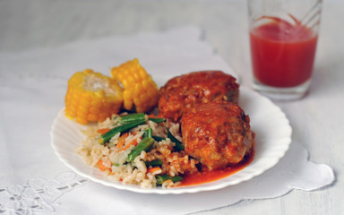 Meat cutlets with tomato sauce, rice and vegetables on a white ceramic plate. Close-up