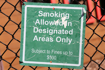 A Green Sign at a Playground that Reads "Smoking Allowed in Designated Areas Only, $500 Fine"