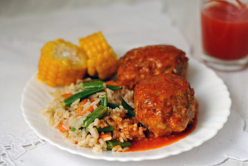 Meat cutlets with tomato sauce, rice and vegetables on a white ceramic plate. Close-up