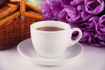 A cup of tea, picnic basket and violet tulips on the table