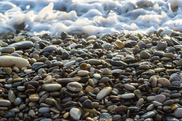 pebble stones on the sea beach, the rolling waves of the sea with foam