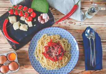 Parmesan, cherry tomatoes, chilli peppers, green cheese and garlic lie on a dark board that stands on a wooden table next to a beautiful plate